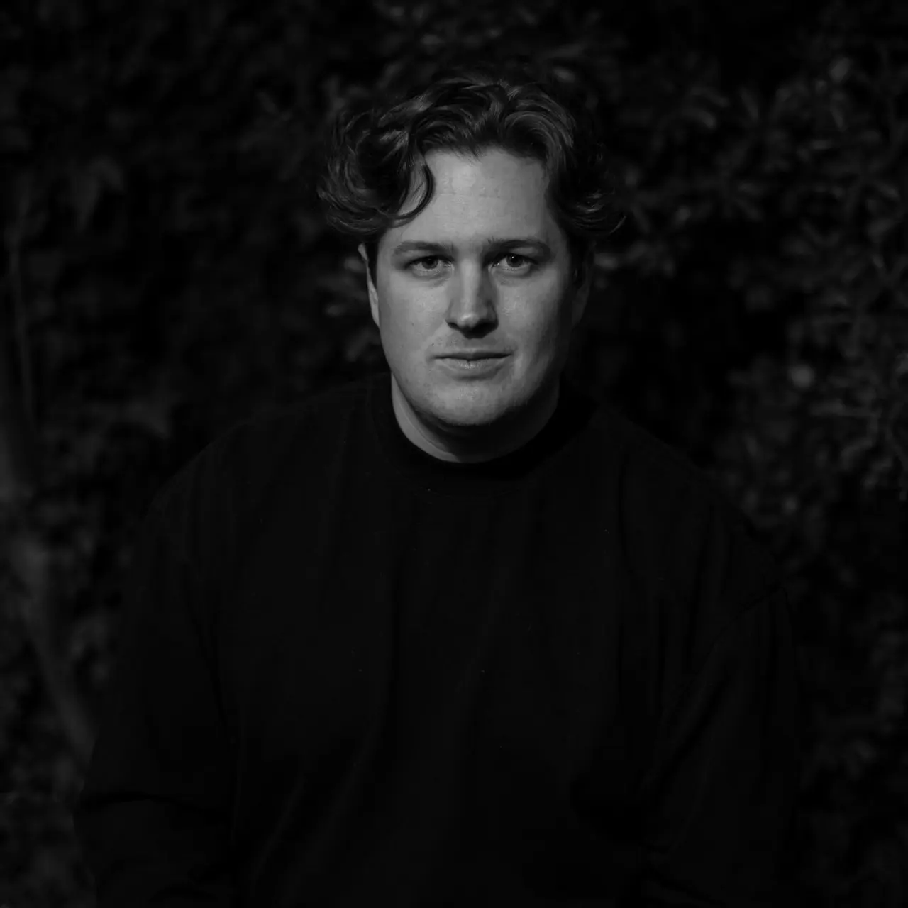 Jake Kenning, lit warmly against dark foliage, in black and white