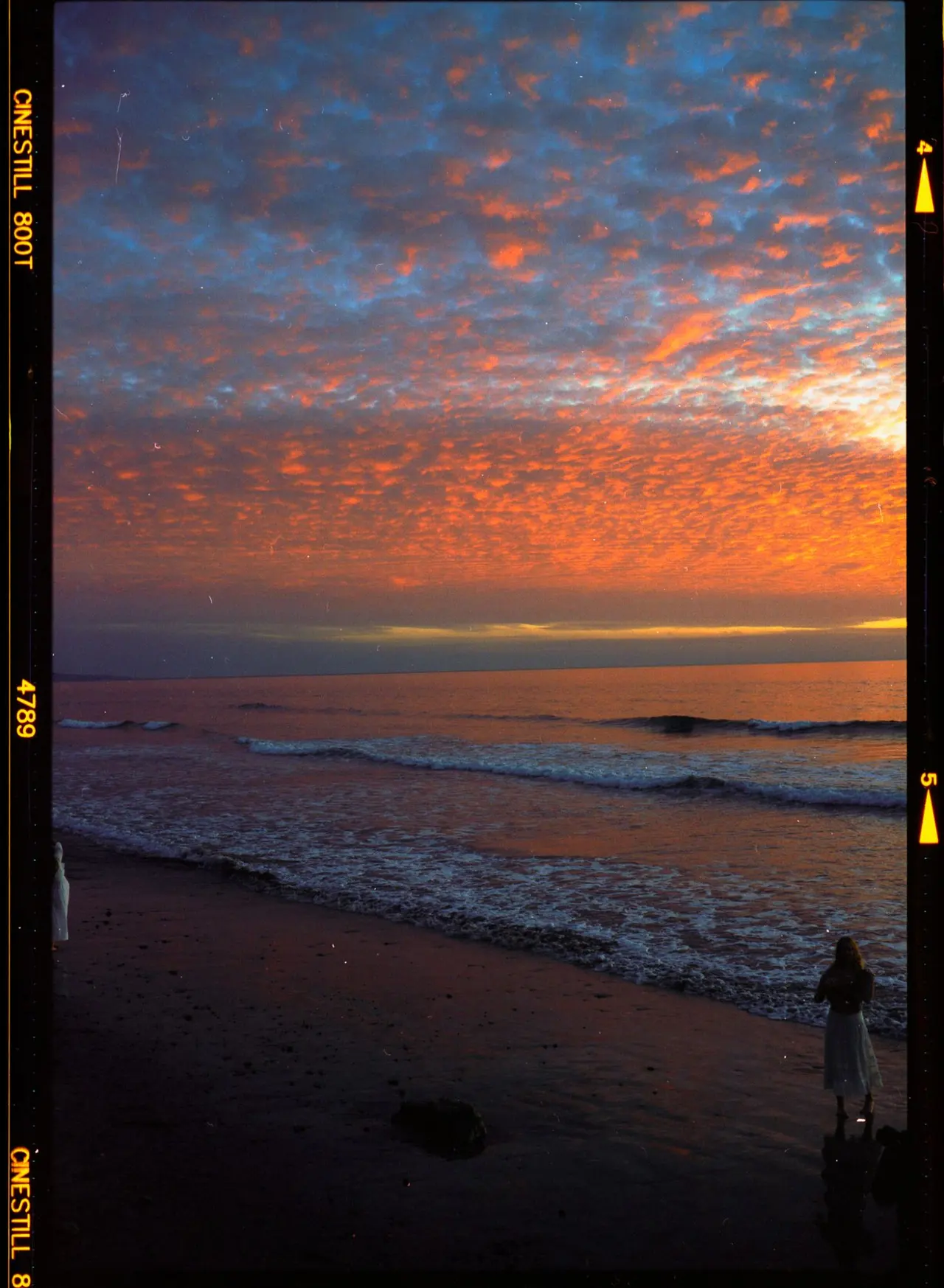 Two figures in white on the sand as the sky burns orange at sunset
